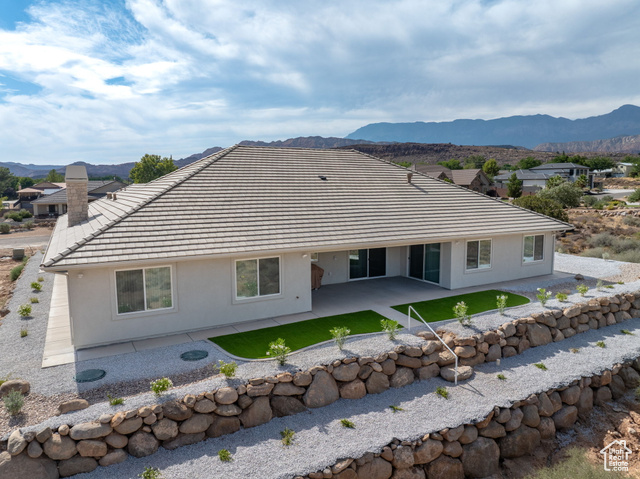 230 Boulder Way Leeds, UT 84746 - Photo 53 of 72 Rear view of property featuring a patio area, stucco siding, terraced rear with stone retaining walls and step down ladders, and a chimney to the wood-burning fireplace in the family room. Concrete sidewalks surround the home.