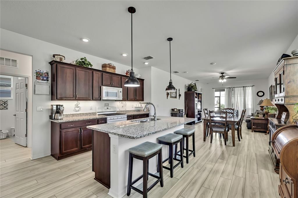 9764 Southwest 100th Avenue Ocala, FL 34481 - Photo 6 of 37 a kitchen with stainless steel appliances granite countertop a stove top oven a sink dishwasher a dining table and chairs with wooden floor