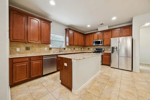 a kitchen with kitchen island granite countertop wooden cabinets stainless steel appliances a sink and a window