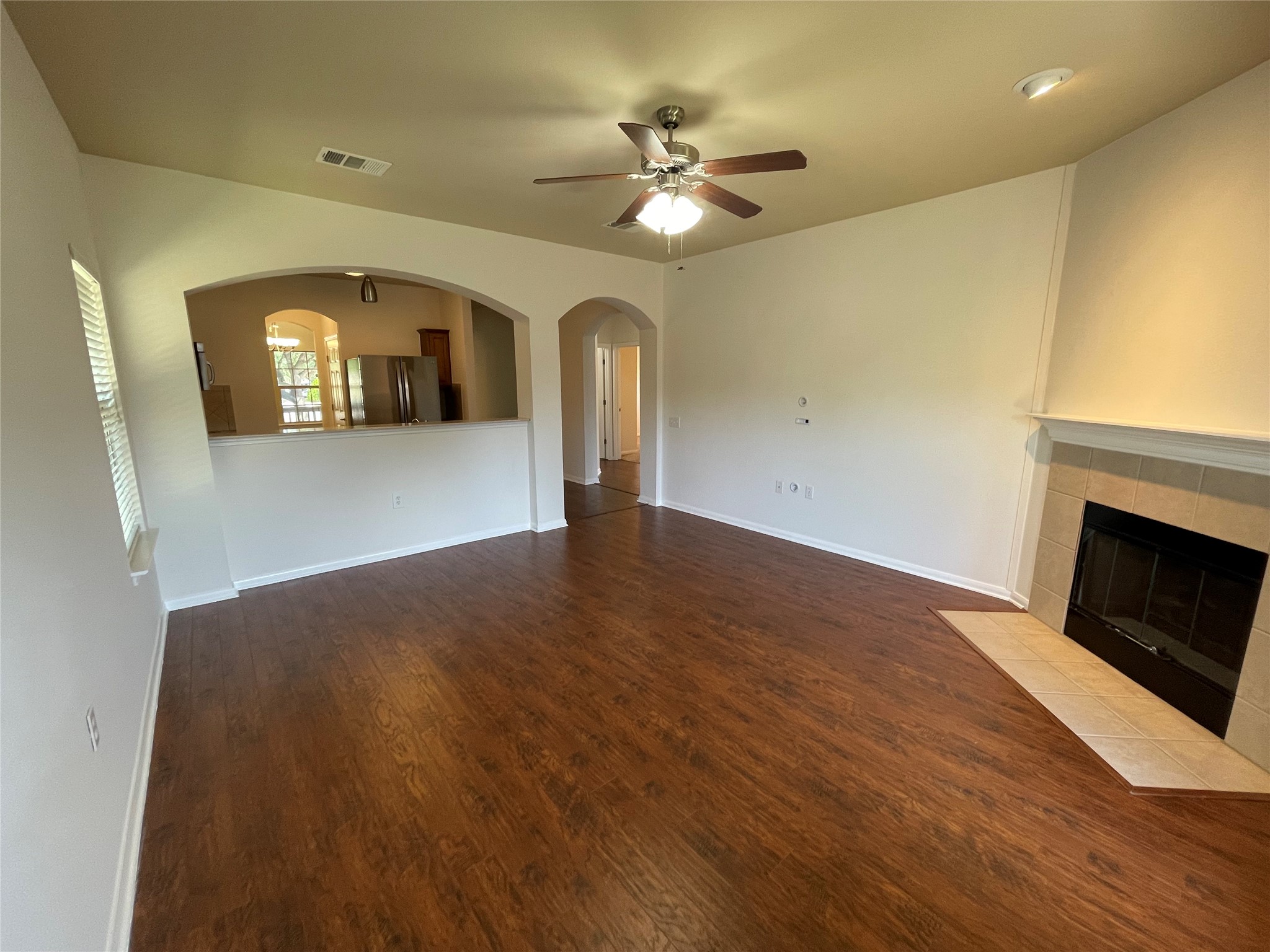 3517 Bronco Bend Loop Austin, TX 78744 - Photo 17 of 39 Unfurnished living room with ceiling fan, dark wood-style flooring, arched walkways, and a tile fireplace