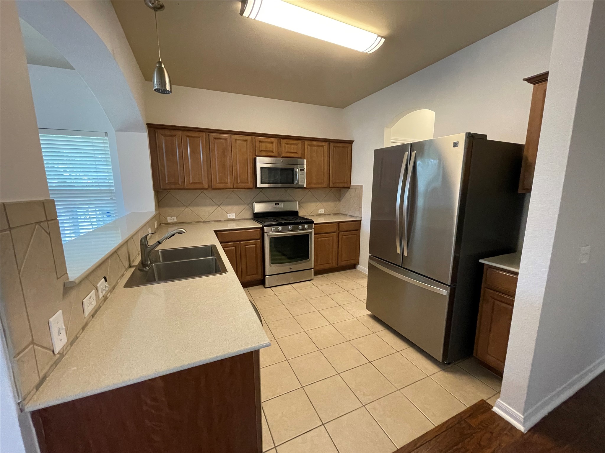 3517 Bronco Bend Loop Austin, TX 78744 - Photo 8 of 39 Kitchen featuring stainless steel appliances, decorative backsplash, light tile patterned floors, wood finish cabinetry, and decorative light fixtures