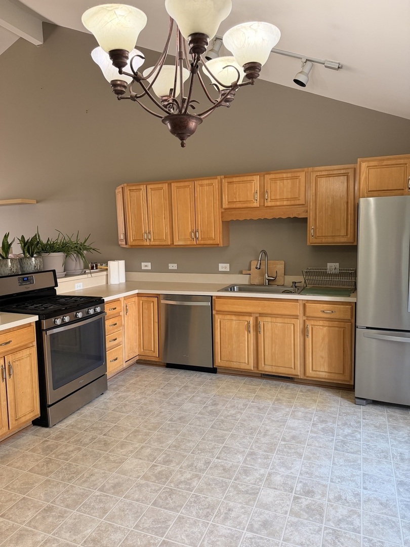 701 Davidson Drive, Unit B Minooka, IL 60447 - Photo 5 of 16 a kitchen with stainless steel appliances granite countertop a sink a stove top oven a chimney cabinets and a dining table