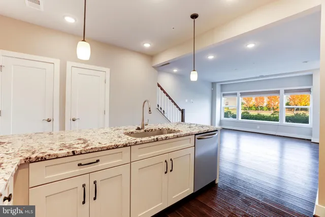 a kitchen with kitchen island granite countertop a stove a sink and white cabinets with wooden floor