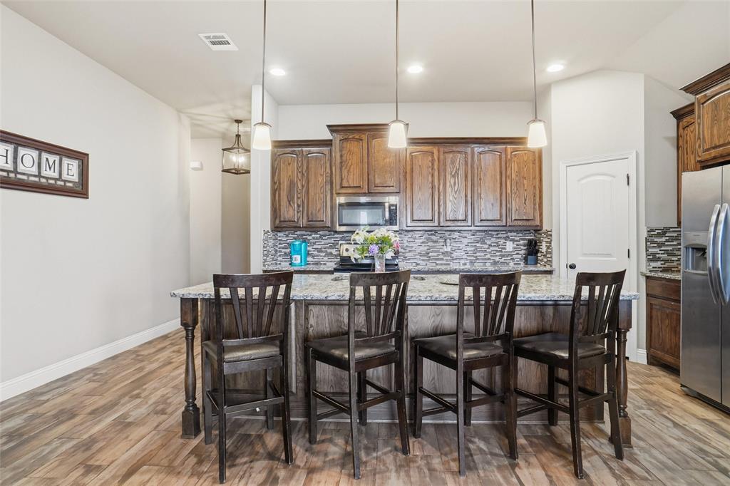 206 McKittrick Lane Godley, TX 76044 - Photo 7 of 28 Kitchen with tasteful backsplash, decorative light fixtures, a center island, light wood-style flooring, and light stone counters
