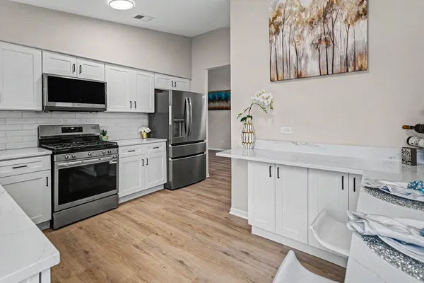 a kitchen with stainless steel appliances a stove top oven a sink a refrigerator white cabinets and wooden floor