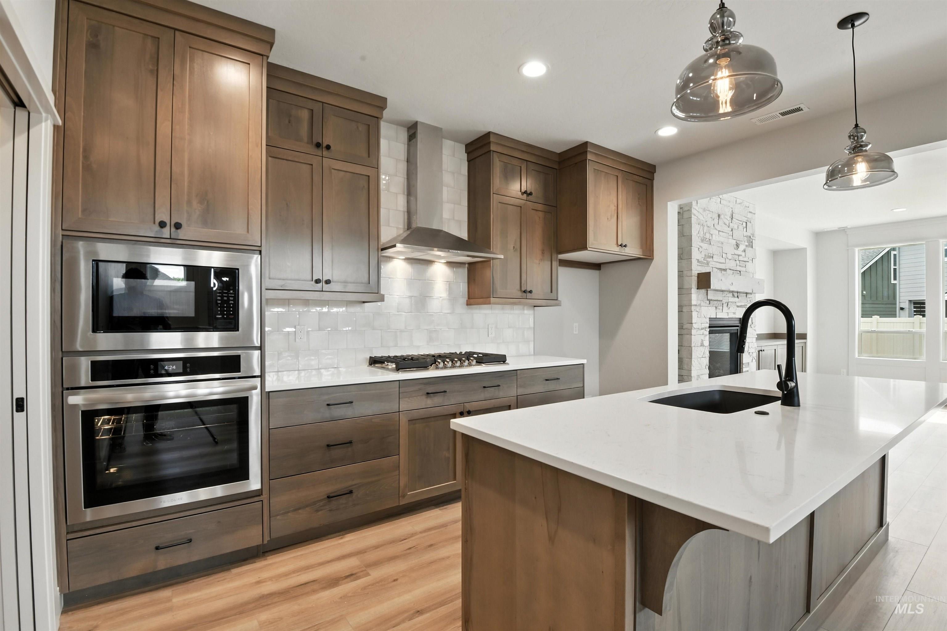 3521 South El Rio Avenue Boise, ID 83709 - Photo 17 of 38 Kitchen with appliances with stainless steel finishes, wall chimney range hood, backsplash, light wood-type flooring, and pendant lighting