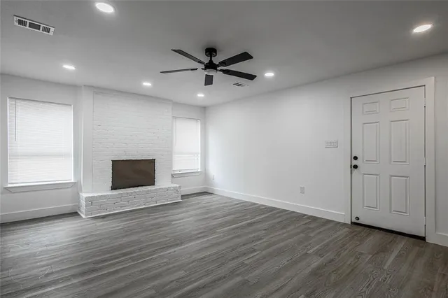 an empty room with wooden floor a ceiling fan a fireplace and windows