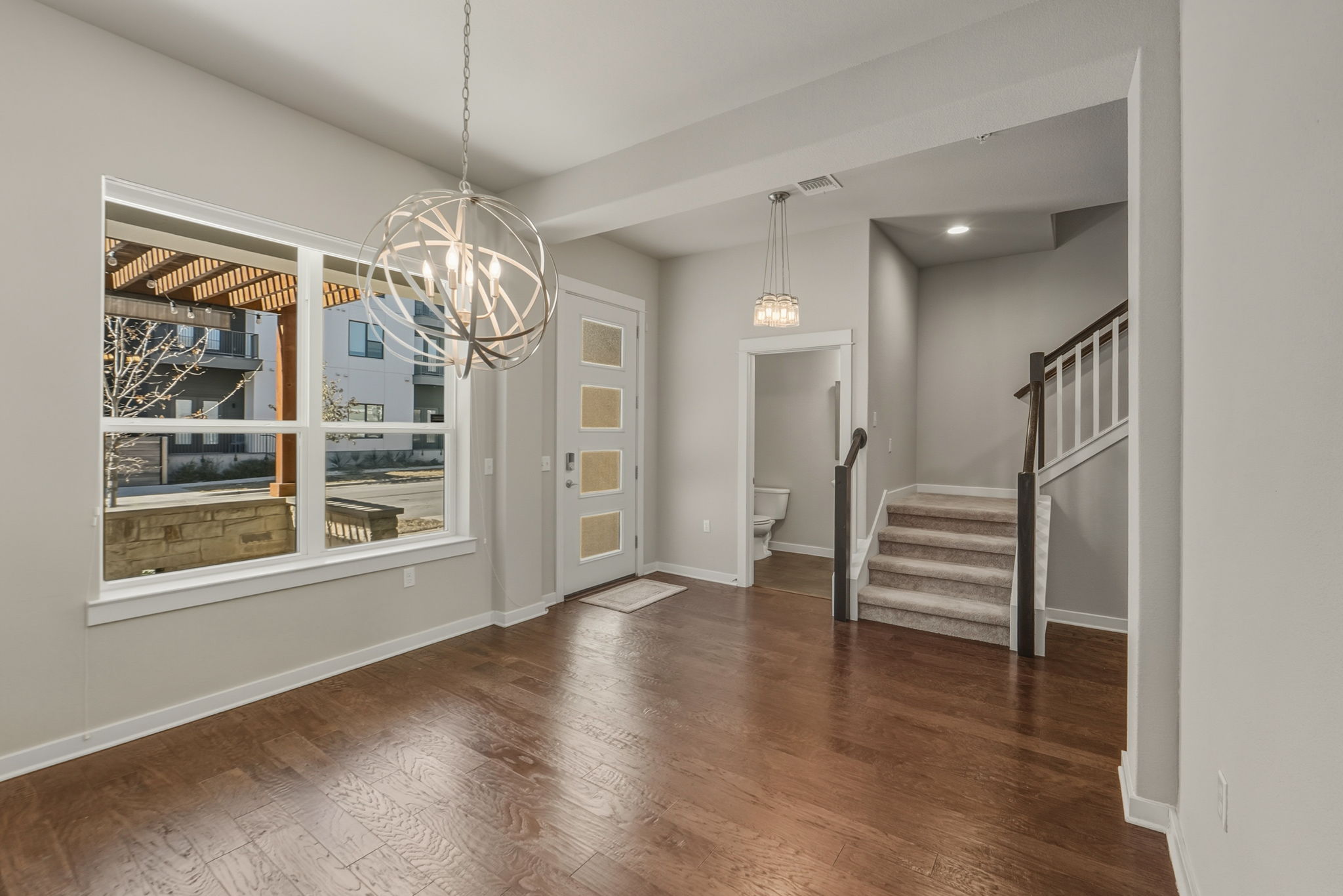 3919 Vaughan Street Austin, TX 78723 - Photo 6 of 40 A striking modern chandelier illuminates rich hardwood floors, complementing the sleek entry door and elegant staircase.