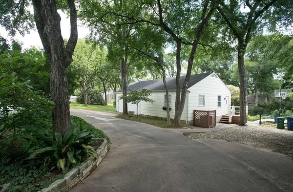 a view of a white house with large trees and plants