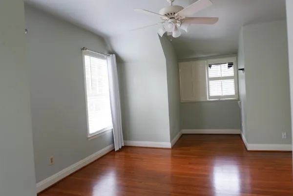 an empty room with wooden floor fan and windows