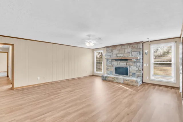 an empty room with wooden floor fireplace and windows