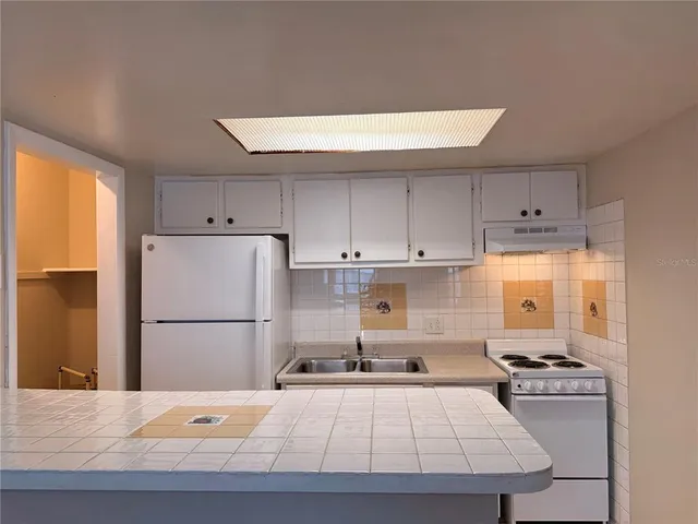 a kitchen with a refrigerator a stove a sink and white cabinets with wooden floor