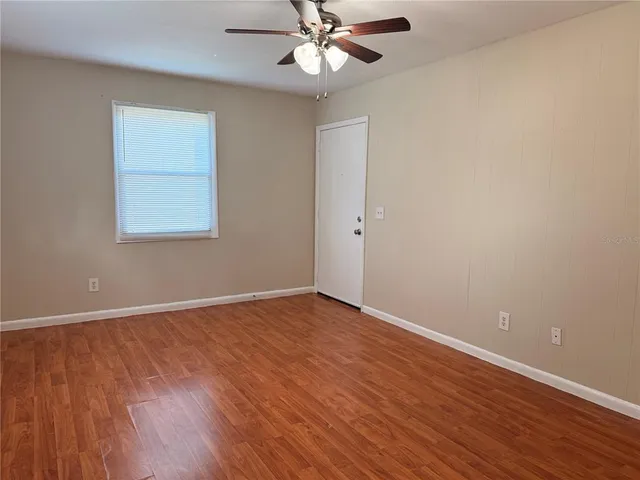 a view of an empty room with wooden floor and a ceiling fan