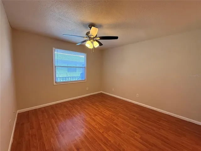 a view of an empty room with chandelier fan and wooden floor
