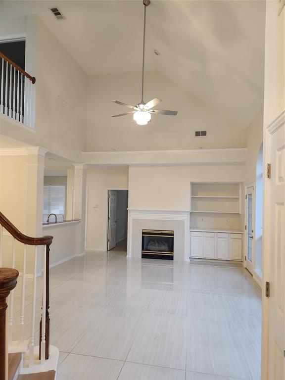 4175 Midrose Trail Dallas, TX 75287 - Photo 3 of 14 Vaulted ceiling living area featuring light-toned tile flooring, a fireplace with a mantel, built-in shelving, white cabinetry, and a ceiling fan with integrated lighting