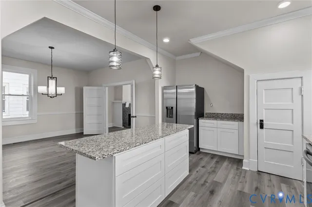 a large kitchen with kitchen island a stove a refrigerator wooden floor and a chandelier