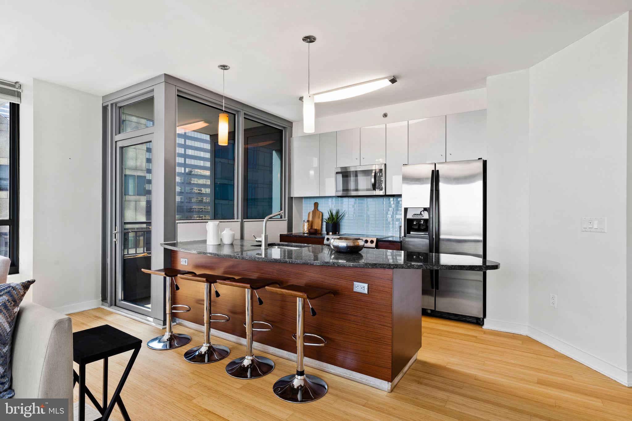 2101 Market Street, Unit 2007 Philadelphia, PA 19103 - Photo 4 of 45 a kitchen with kitchen island a stove a refrigerator and a dining table with wooden floor