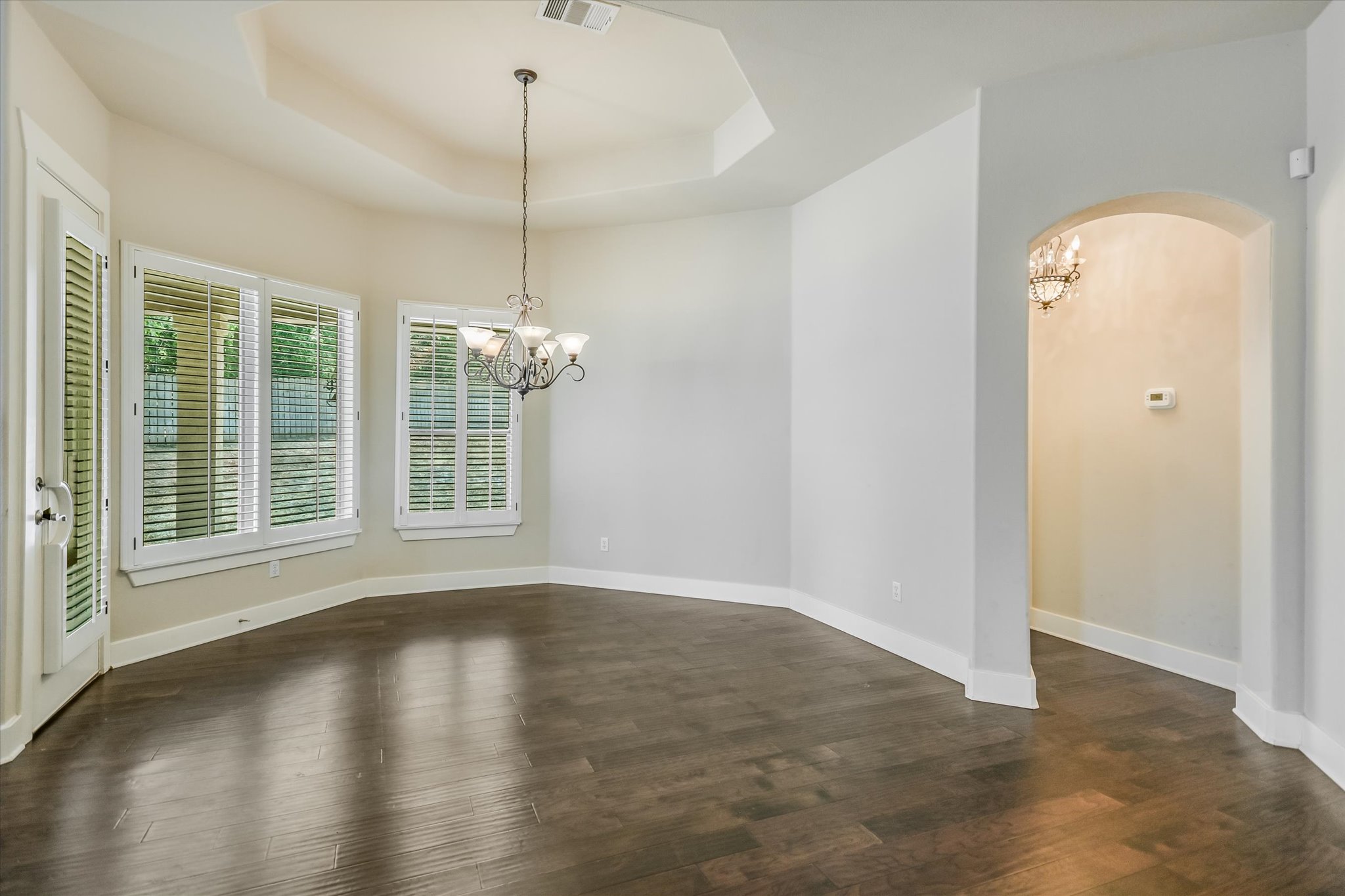 210 Rivulet Lane Austin, TX 78738 - Photo 12 of 20 Unfurnished dining area featuring a chandelier, a tray ceiling, dark wood-style flooring, and arched walkways