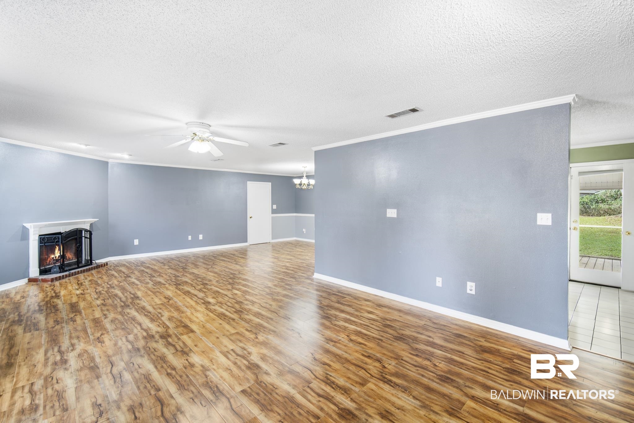 103 Ann Street Daphne, AL 36527 - Photo 3 of 23 Unfurnished living room featuring crown molding, wood finished floors, a warm lit fireplace, ceiling fan, and a textured ceiling