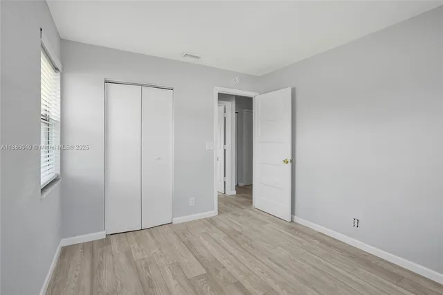 a view of an empty room with wooden floor and closet area
