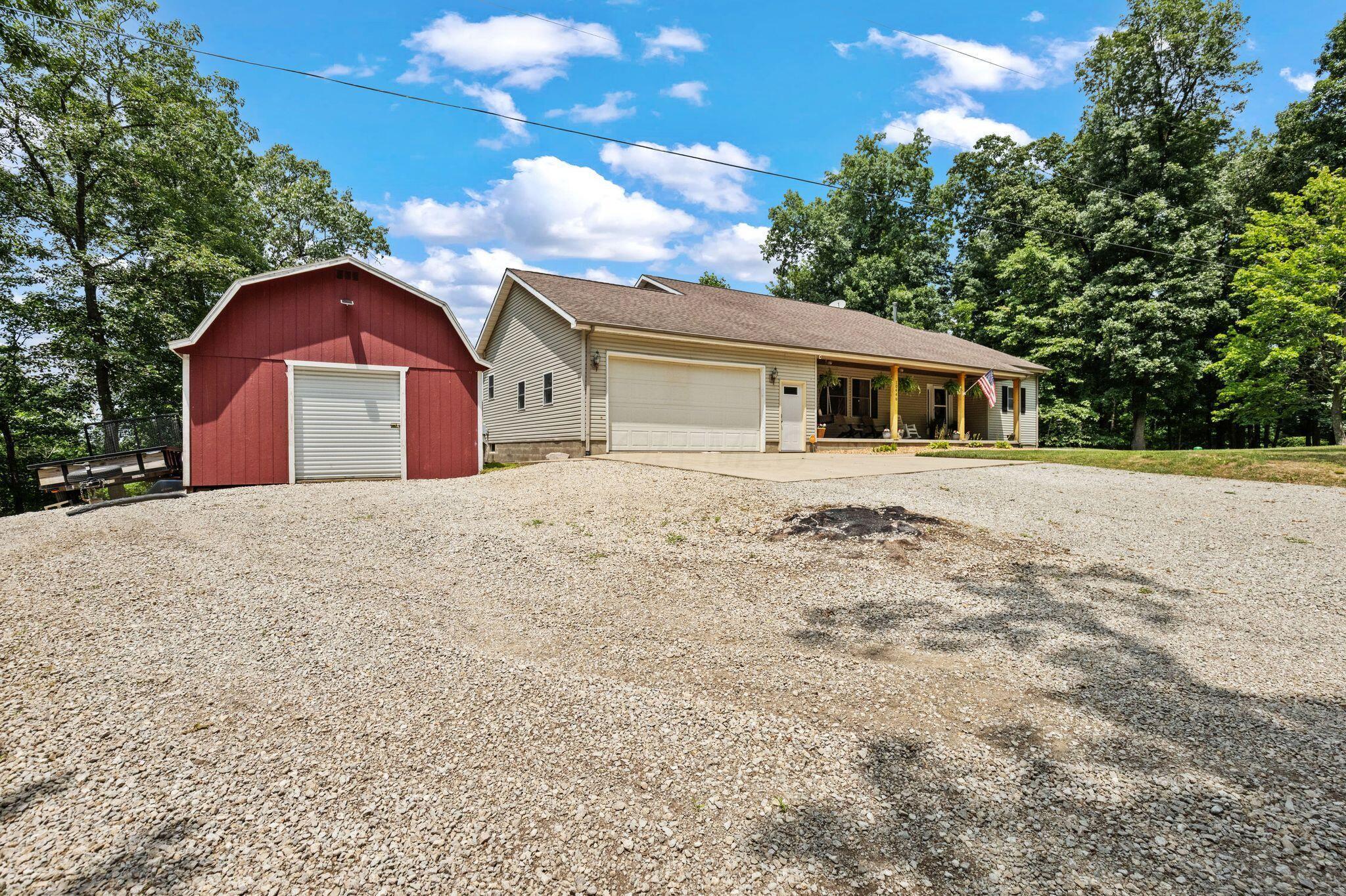 10446 Rich Hollow Road Southwest Lancaster, OH 43130 - Photo 69 of 83 Property exterior featuring a detached red barn, a gravel driveway, an attached garage, a covered front porch with wooden support columns, and surrounding mature trees