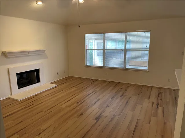 a view of an empty room with wooden floor fireplace and a window