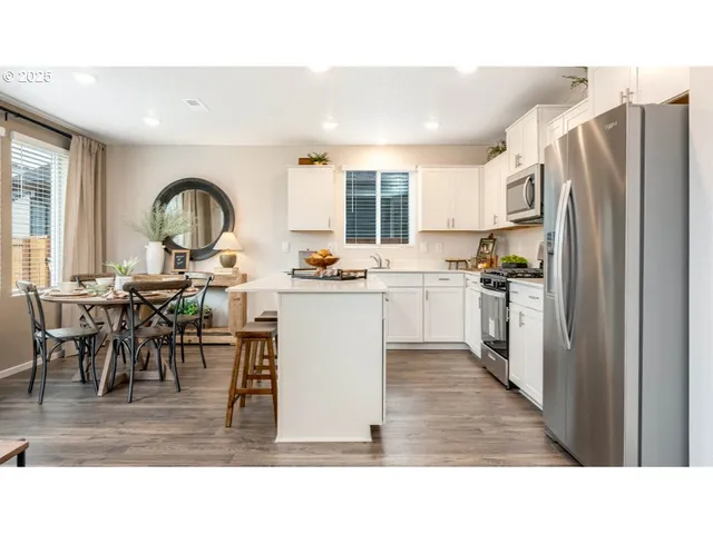 a open kitchen with stainless steel appliances granite countertop a refrigerator a stove a sink and a dining table with wooden floor