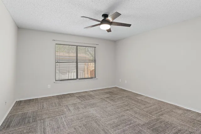 an empty room with chandelier fan and windows
