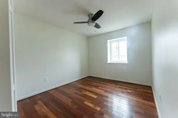 an empty room with wooden floor ceiling fan and windows
