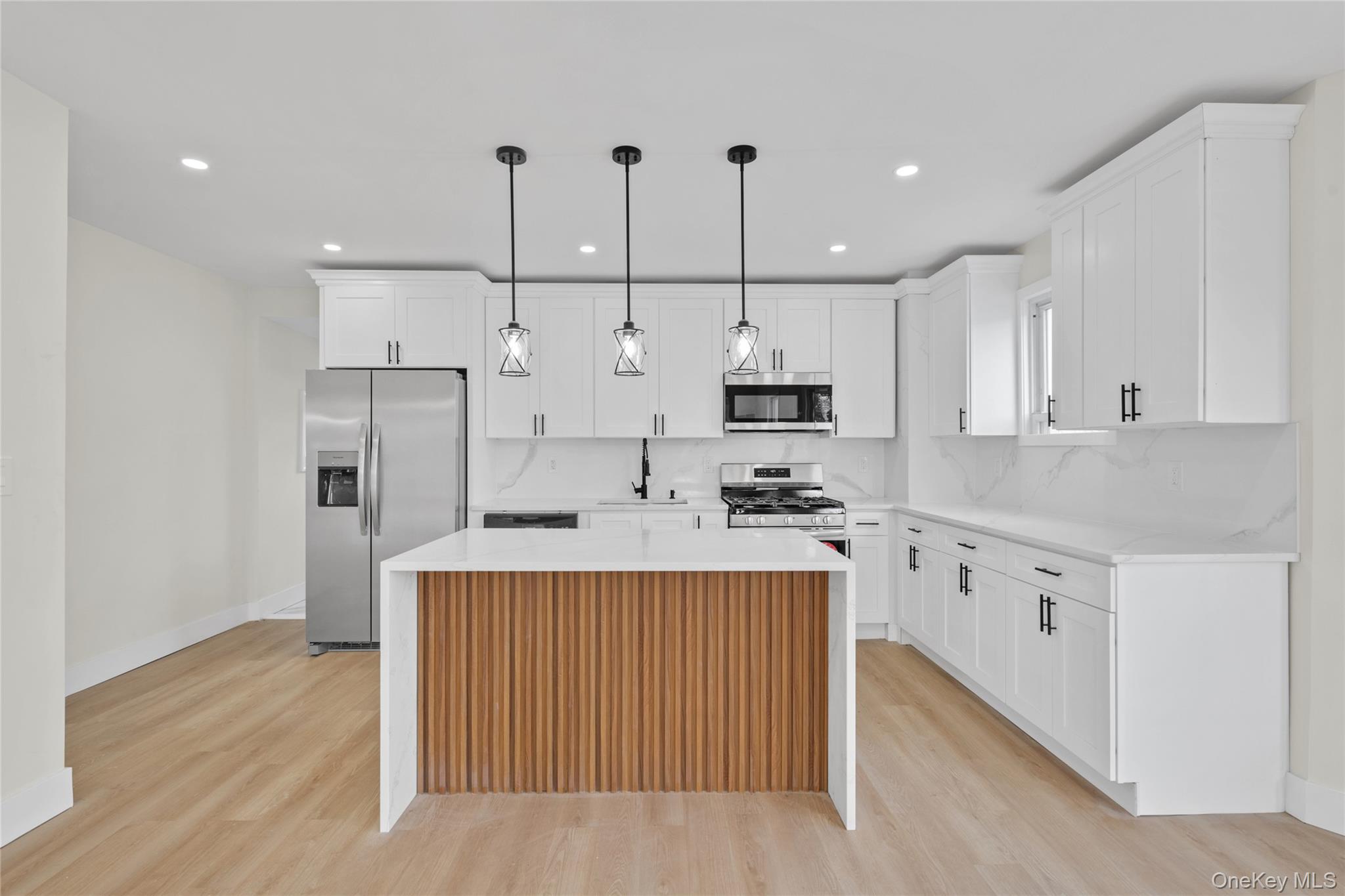 220-27 134th Road Queens, NY 11413 - Photo 5 of 22 Kitchen with a kitchen island, appliances with stainless steel finishes, light stone counters, decorative light fixtures, and light wood finished floors