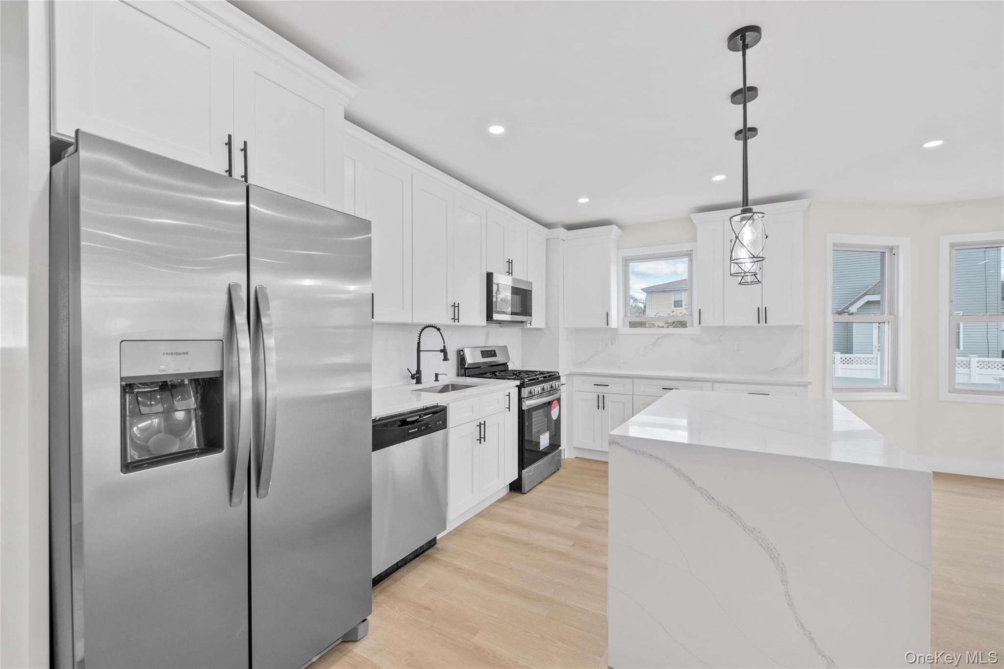 220-27 134th Road Queens, NY 11413 - Photo 6 of 22 Kitchen featuring stainless steel appliances, light stone counters, light wood-style flooring, pendant lighting, and white cabinetry