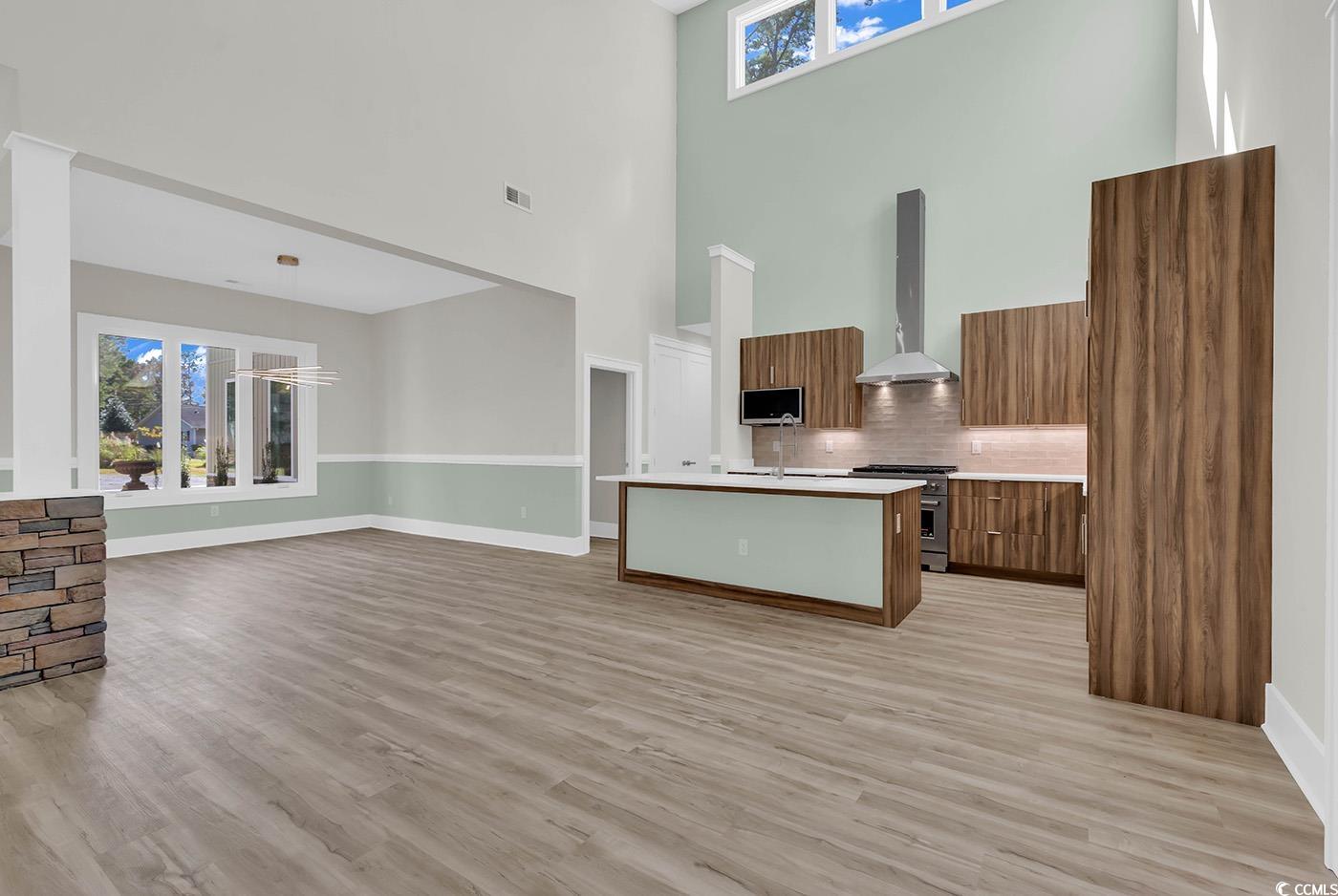 1028 Colette Court Conway, SC 29526 - Photo 3 of 39 Kitchen featuring healthy amount of natural light, brown cabinetry, modern cabinets, wall chimney range hood, and a towering ceiling