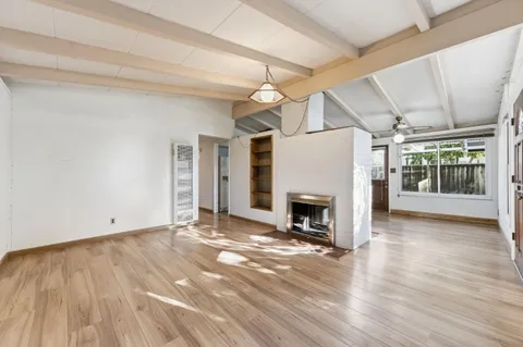 an empty room with wooden floor fireplace and windows