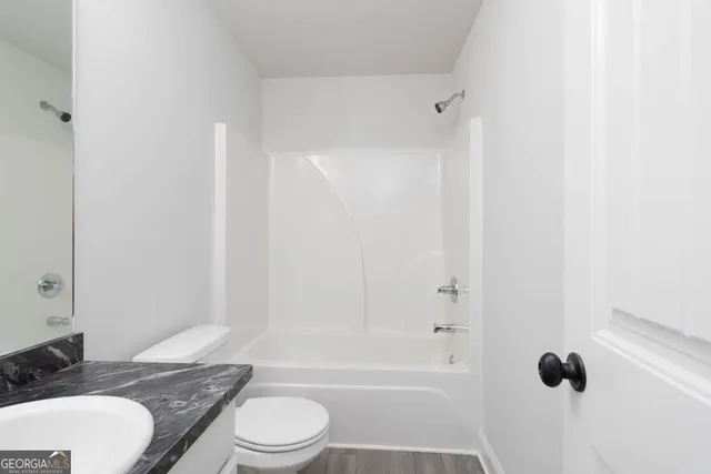 a bathroom with a granite countertop bathtub shower sink vanity mirror and toilet