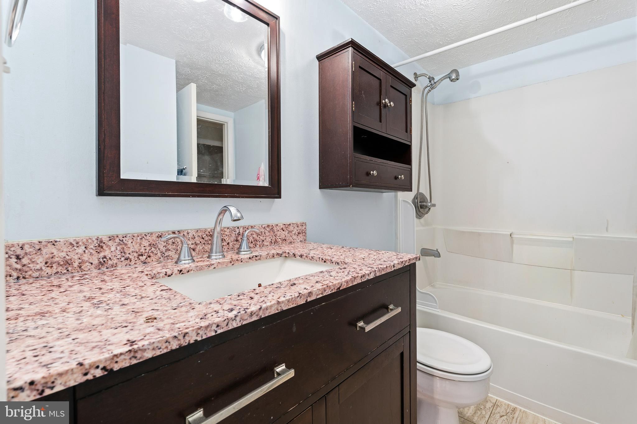 19218 Misty Meadow Terrace Germantown, MD 20874 - Photo 15 of 17 a bathroom with a granite countertop sink a toilet a mirror and bathtub