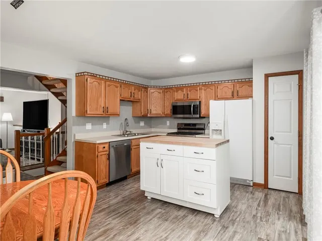 a large kitchen with stainless steel appliances granite countertop a stove a sink a refrigerator and white cabinets with wooden floor