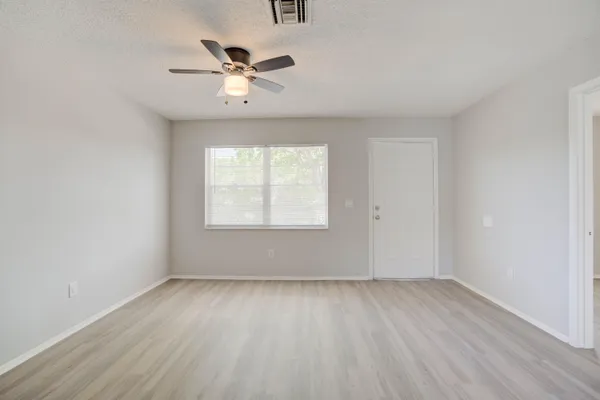 an empty room with wooden floor chandelier fan and windows