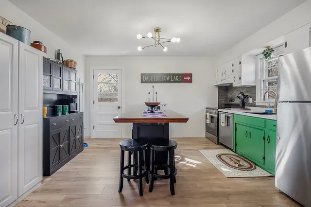a kitchen with stainless steel appliances kitchen island granite countertop a refrigerator a sink dishwasher a dining table and chairs with wooden floor