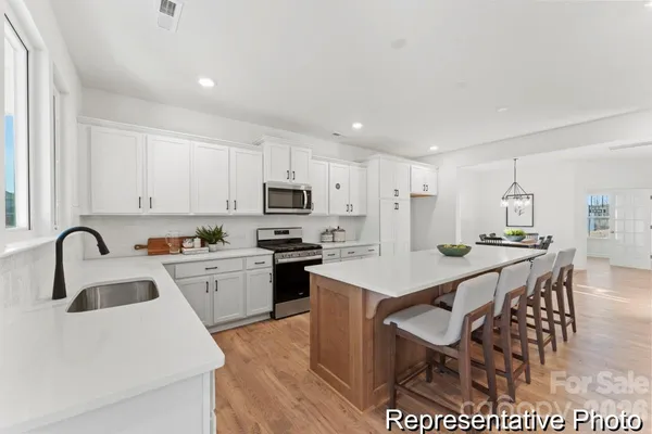 a kitchen with stainless steel appliances kitchen island granite countertop a sink a stove a dining table and chairs with wooden floor