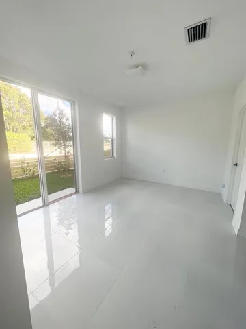 an empty room with windows and view of kitchen