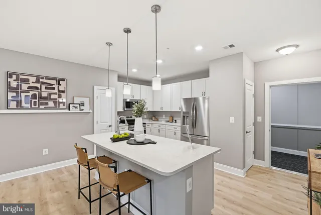 a kitchen with stainless steel appliances kitchen island granite countertop a refrigerator a microwave oven a dining table and chairs with wooden floor