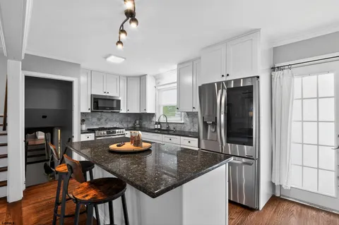 a kitchen with stainless steel appliances granite countertop a refrigerator a stove a sink a dining table and chairs with wooden floor