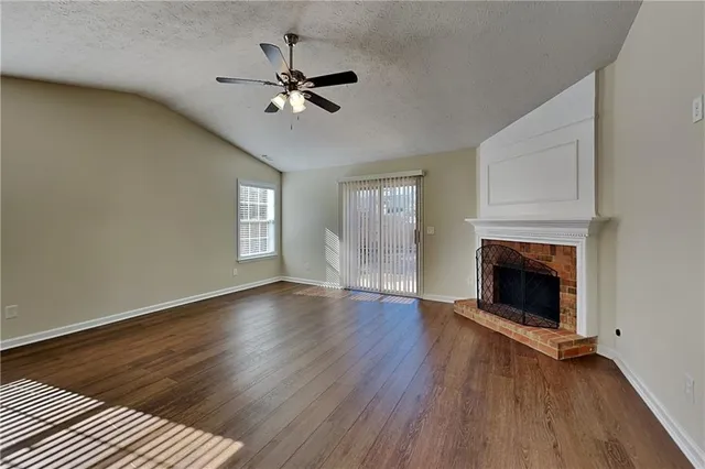 a view of an empty room with wooden floor fireplace and a window