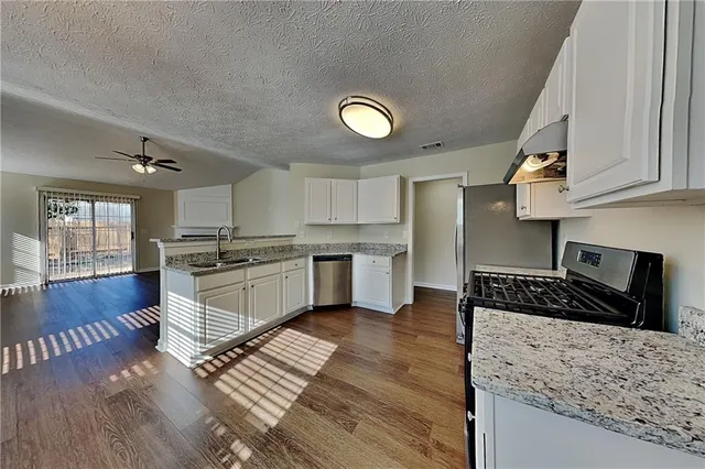 a kitchen with granite countertop a stove top oven a sink dishwasher and white cabinets with wooden floor