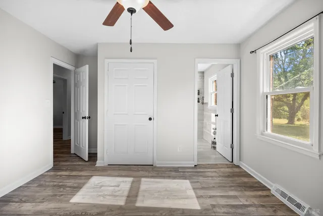 an empty room with wooden floor fan and windows