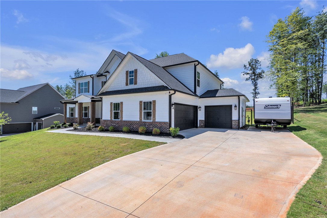 226 Holly Br Road Piedmont, SC 29673 - Photo 3 of 44 A newly constructed residence features an attached three-car garage and a wide concrete driveway, nestled within a verdant setting.
