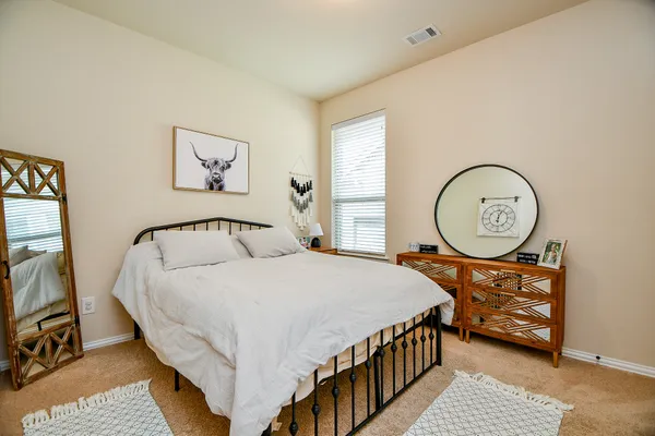 a bedroom with a bed a mirror on the dresser and a window