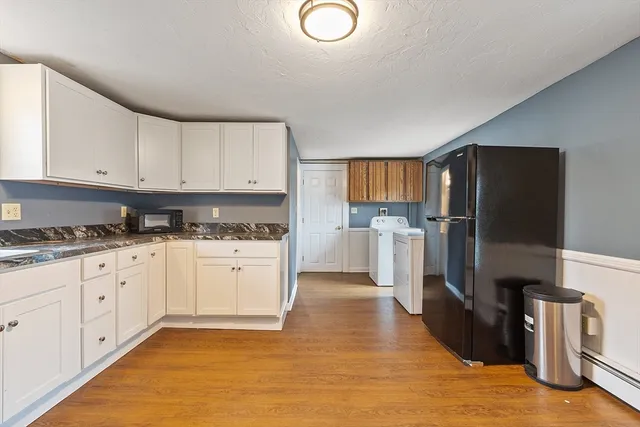 a kitchen with granite countertop a refrigerator oven a sink dishwasher and white cabinets next to a window