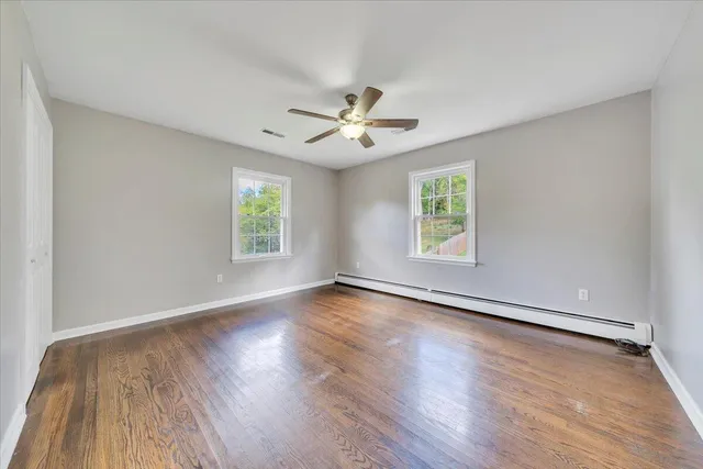 an empty room with wooden floor ceiling fan with window