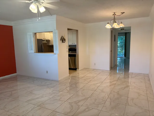 an empty room that has a chandelier fan and kitchen view